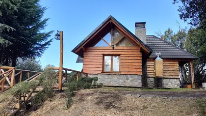 Fachada de cabaña rústica de madera con base de piedra y ventanas grandes — proyecto Teja Gravillada., por Yrigoyen Construcciones, en Córdoba